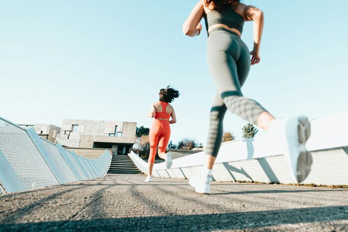 Two women running outdoors on a sunny day, with clear sky and modern architecture in the background, focus on movement.