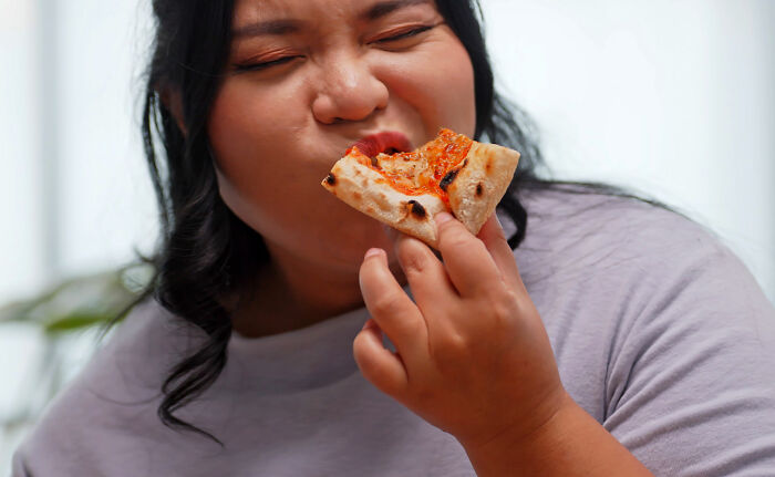 Person enjoying a slice of pizza, illustrating challenges faced by ex-fat people trying to lose weight.