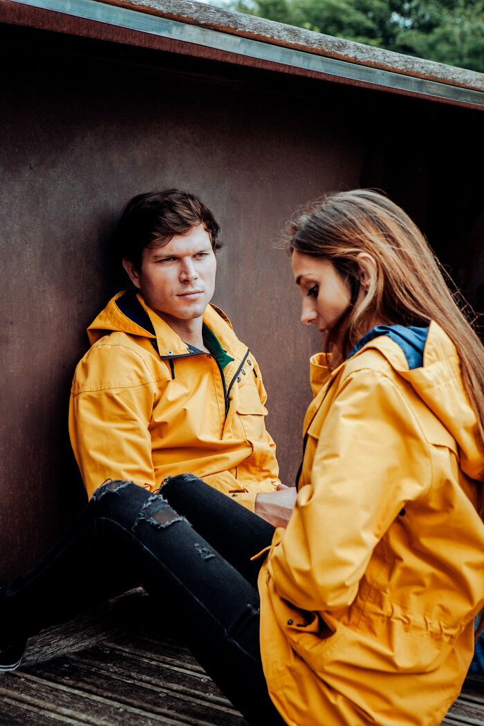 A man and woman wearing yellow jackets sitting apart, depicting a moment of emotional rejection or tension.
