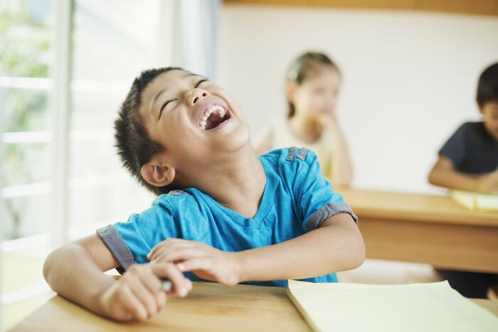 Boy laughing joyfully in classroom setting, representing stories of people getting savagely rejected in love and relationships.
