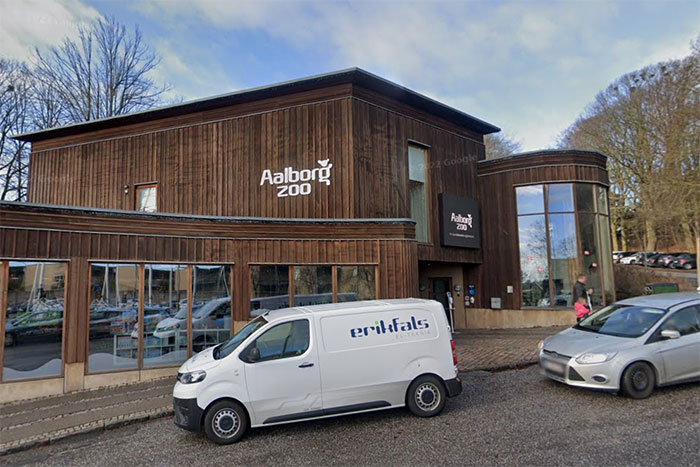 Aalborg Zoo entrance with parked vehicles outside on a clear day, relating to donation and lions topic.