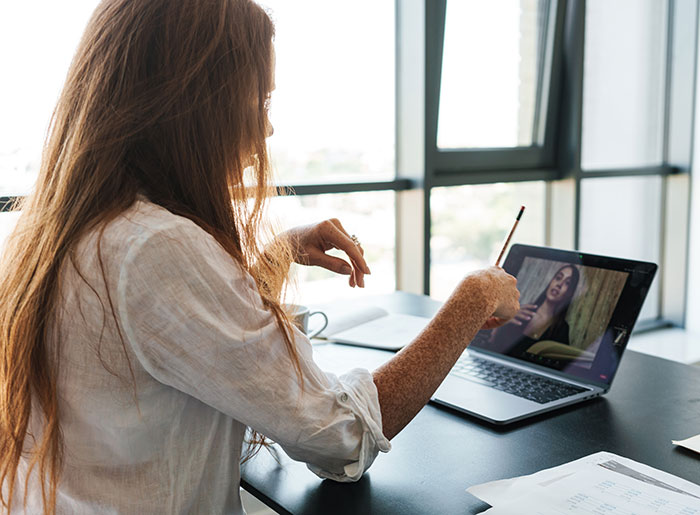 Woman receiving an email about a second interview while watching a video file on her laptop at a desk near a window.