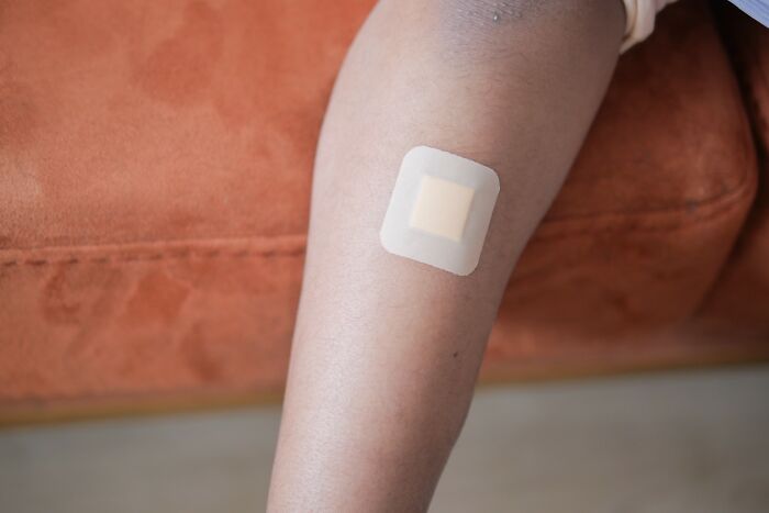 Close-up of a forearm with a small adhesive bandage applied, representing autopsy tech safety and injury prevention. - 12