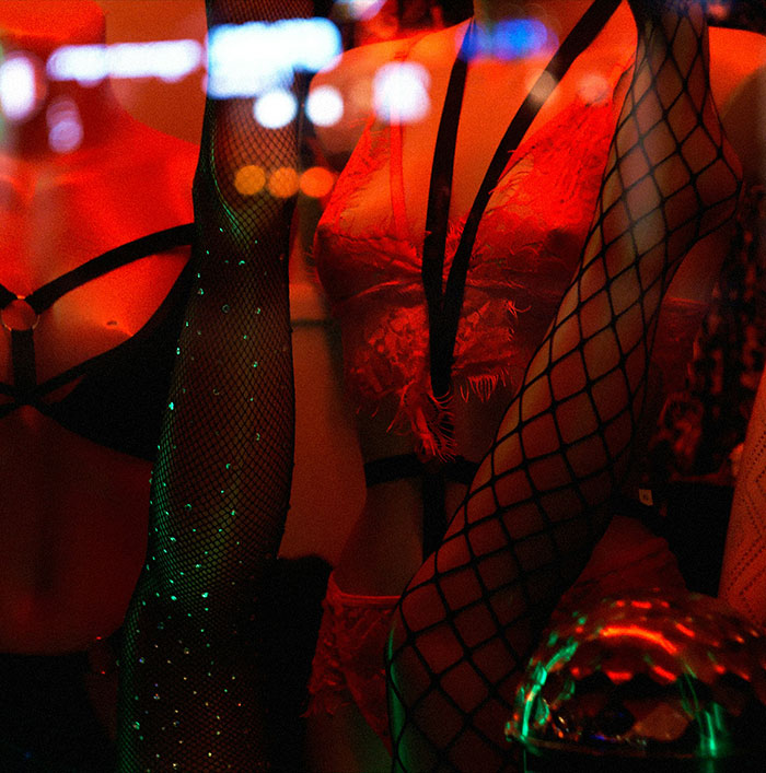 Women in fishnet stockings and lingerie under red lighting illustrating brothel manager exposing ways men get caught by partners. - 8