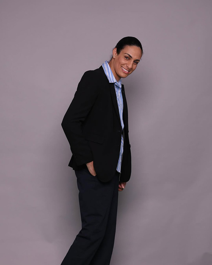 Imane Khelif posing with a smile in a black blazer and striped shirt showing a dramatic makeover after gender controversy.