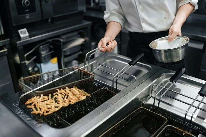 Chef frying French fries in a professional kitchen, demonstrating profession secrets in food preparation and cooking techniques.