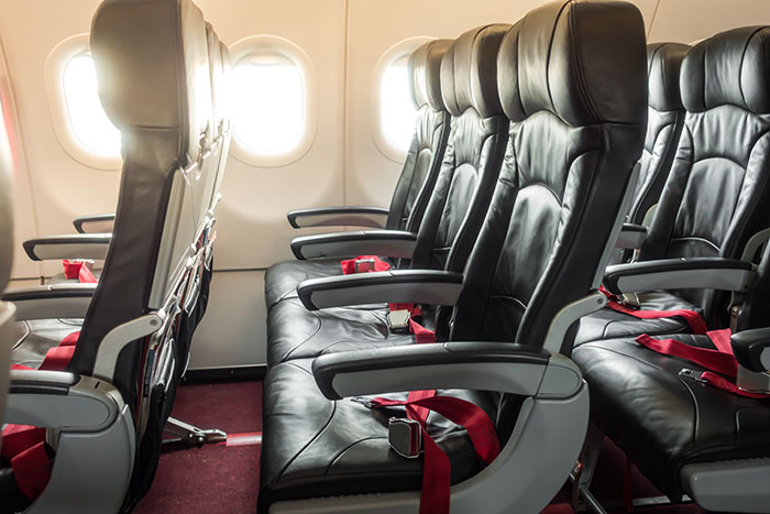 Empty airplane seats with red seatbelts in a cabin, illustrating a mom&rsquo;s vent about a 6-leg flight with a traumatized kid.