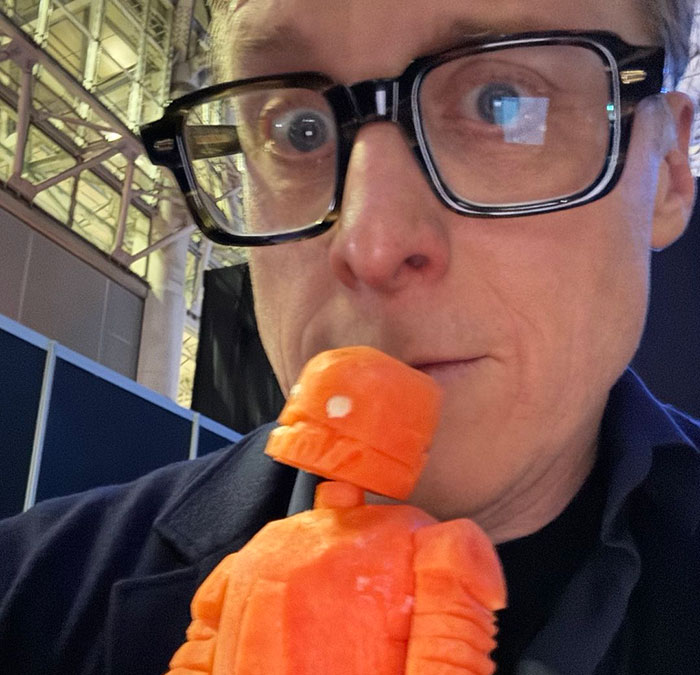 Co-actor wearing glasses holding an orange figurine, related to studio removing his name from publicity claims.