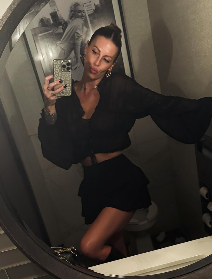 Mom with over 30 tattoos taking a mirror selfie wearing a black outfit, showing her tattooed arm and stylish look.