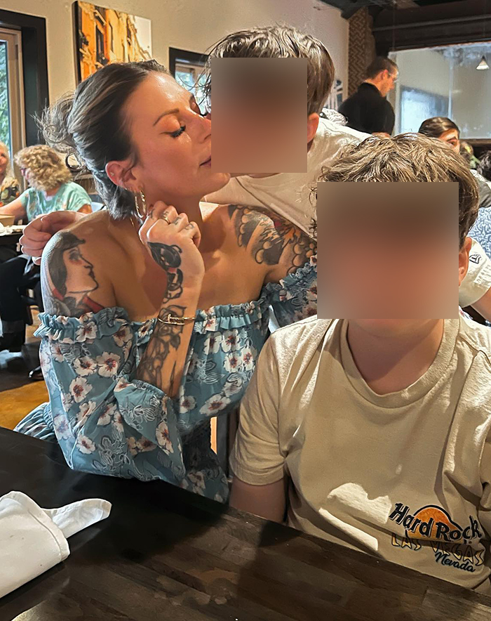 Mom with over 30 tattoos sitting at a table with children in a casual restaurant setting, showing detailed arm tattoos.
