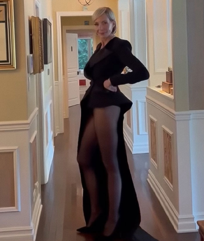 Jamie Lee Curtis wearing a pantless black dress, posing confidently in a hallway with elegant interior decor.