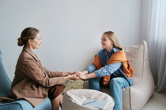 Two women holding hands and smiling in a cozy room, sharing positive moments and good news together.