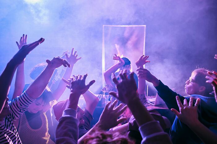 People raising hands and dancing in a crowded club environment under purple lighting, representing gender-based double standards.