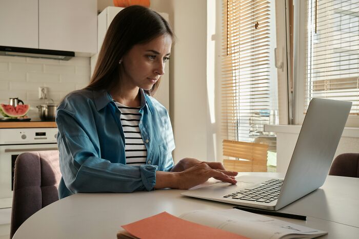 Woman in a blue shirt using a laptop at home, representing netizens discussing aspects of modern life breaking down.