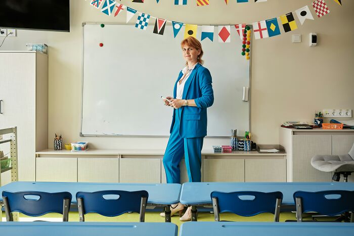 Teacher standing confidently in a classroom decorated with colorful flags, highlighting school kids' wildest confident moments.
