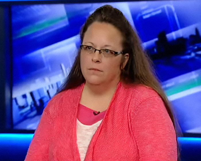 Kim Davis in a news interview wearing glasses and a coral sweater, known as an anti-LGBTQ activist.
