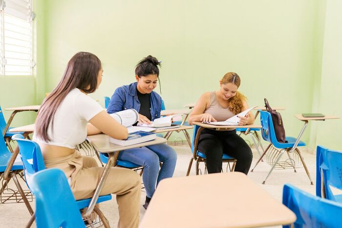 Three students studying together in a classroom, reflecting positive vibes and good news about education and learning environments.