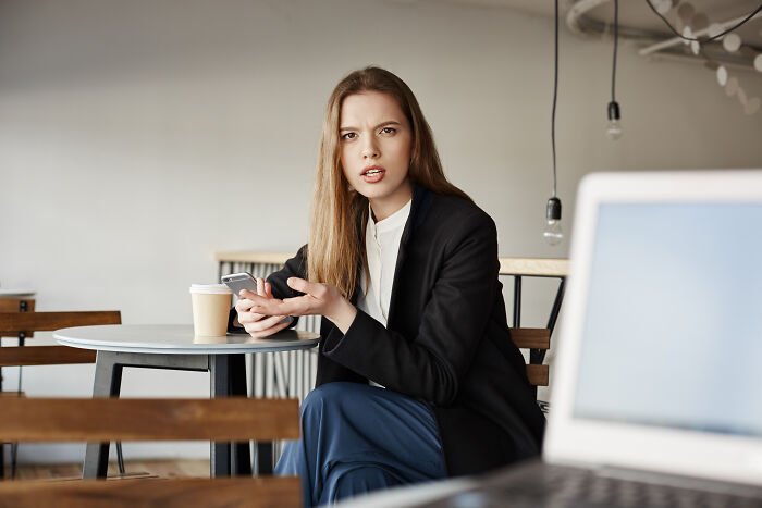 Woman in business attire looking frustrated while holding a phone, depicting hiring managers dealing with difficult people.