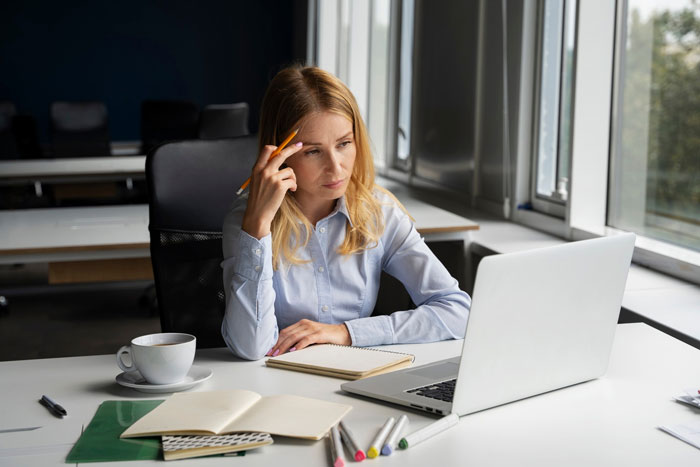 Young female employee sitting at desk looking concerned while using laptop, representing creepy guy incessantly texting scenario. Young female employee sitting at desk looking concerned while using laptop, representing creepy guy incessantly texting scenario.