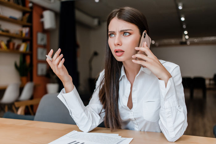 Young woman at work looking frustrated while on phone, representing creepy guy incessantly texting female colleague concerns. Young woman at work looking frustrated while on phone, representing creepy guy incessantly texting female colleague concerns.
