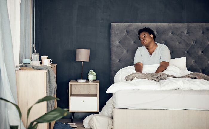Person sitting on bed in a modern bedroom, appearing thoughtful while sharing weight loss tips for ex-fat individuals.