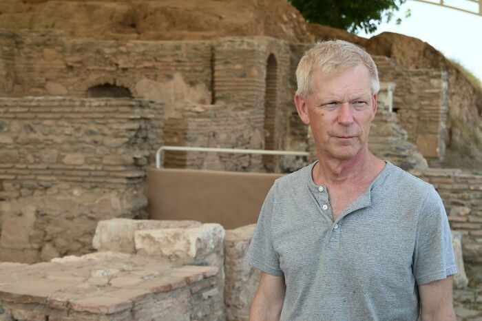 Middle-aged man standing near ancient stone ruins of a Lydian palace site in western T&uuml;rkiye archaeological excavation.