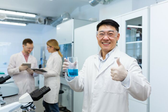 Scientist in a lab giving thumbs up while holding a blue liquid, representing the smartest kids in their class success.