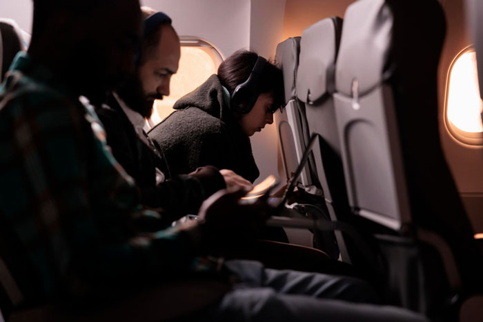 Woman pretending to be asleep in airplane aisle seat, refusing to move while other passengers sit nearby. Woman pretending to be asleep in airplane aisle seat, refusing to move while other passengers sit nearby.