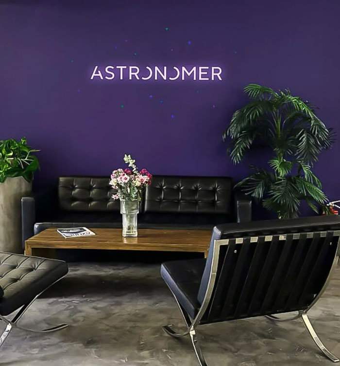 Modern office lounge with black leather seating, plants, and a vase of flowers under the Astronomer logo wall. Modern office lounge with black leather seating, plants, and a vase of flowers under the Astronomer logo wall.