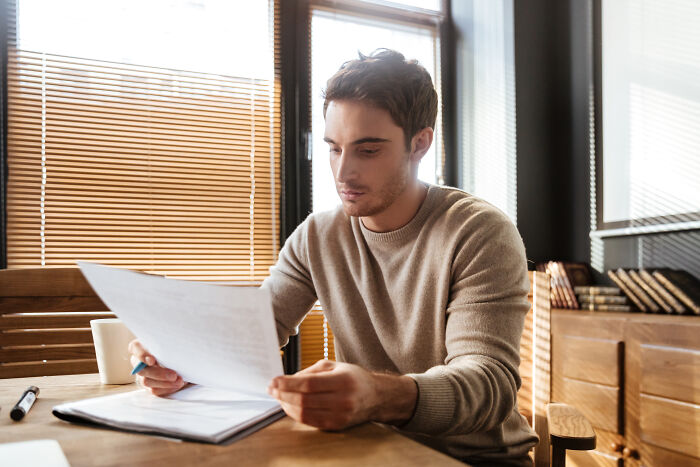 Young man in a cozy room reading documents, focused on discovering profession secrets for career growth and success.