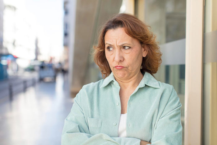 Middle-aged woman with crossed arms looking displeased outdoors, representing aunt ignoring nephew until he gets job.