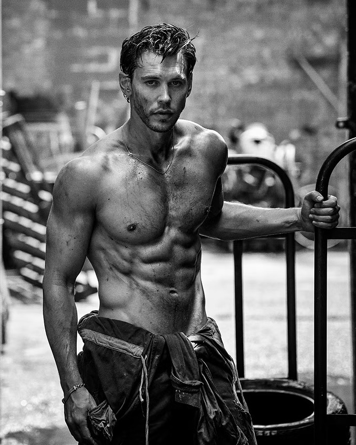 Austin Butler in a shirtless photoshoot showcasing peak male body and muscular physique in a gritty urban setting.