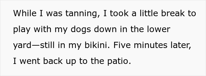 Woman wearing bikini in her own yard playing with dogs during a tanning break near the patio area.