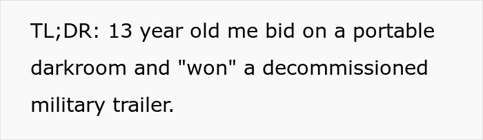 Teen holding a bid paddle beside a large decommissioned military trailer won at surplus auction.