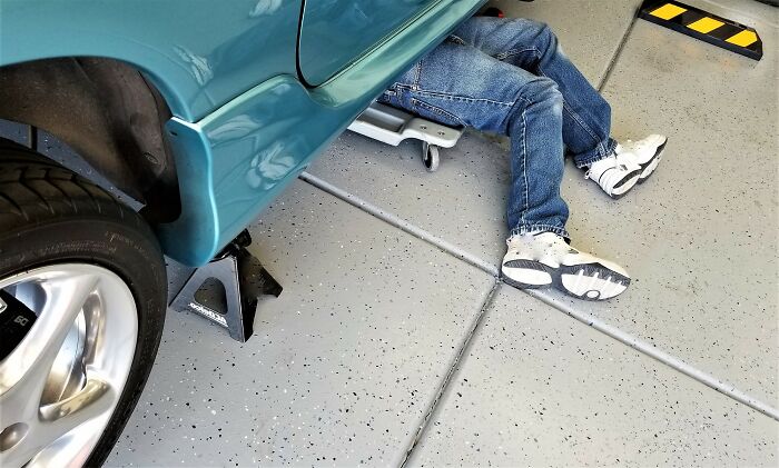Person working under a car in a garage, illustrating risks to avoid to prevent ending up on an autopsy tech’s table. - 2