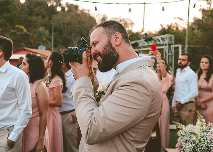 Man in beige suit taking photos at a wedding, highlighting critique of expensive wedding photographer service.