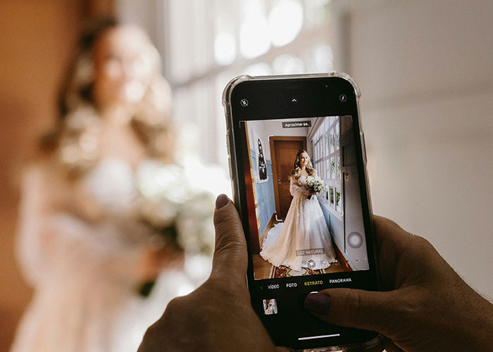 Bride captured on smartphone in wedding dress, highlighting a $3K wedding photographer criticism in a home setting.
