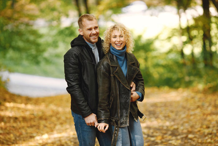 Couple walking in autumn park, smiling and enjoying the outdoors, illustrating parents obsessed with having kids.