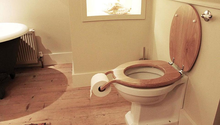Toilet with wooden seat designed to hold toilet paper, showing a clear example of design fails in household items.