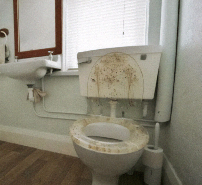 Dirty toilet with stained seat and tank in a bathroom highlighting design fails and poor maintenance.