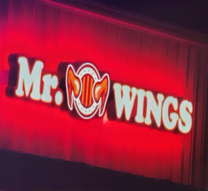 Neon sign with a design fail showing "Mr. Pig Wings" instead of a clear restaurant name in bright red lighting.