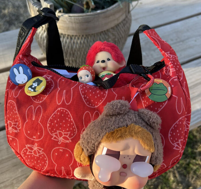 Red bag with strawberry and bunny patterns, decorated with playful pins and toys, showcasing school kids creativity and confidence.