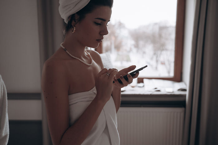 Young woman wrapped in towel using smartphone by a window, evoking a sense of terrifying true stories and no regrets.