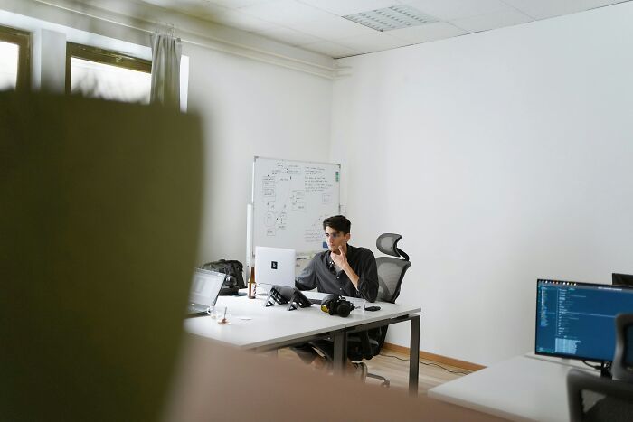 Young man working at desk with laptop and camera in modern office, representing strange money-making hacks ideas.