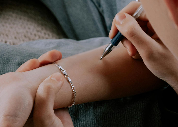 Close-up of a person writing on their forearm with a pen, illustrating unhinged mom hacks toe the line between genius and chaos.