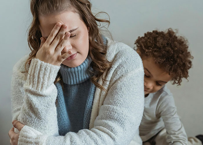 Stressed mom with hand on forehead while child playfully hugs her, showing chaos of unhinged mom hacks.