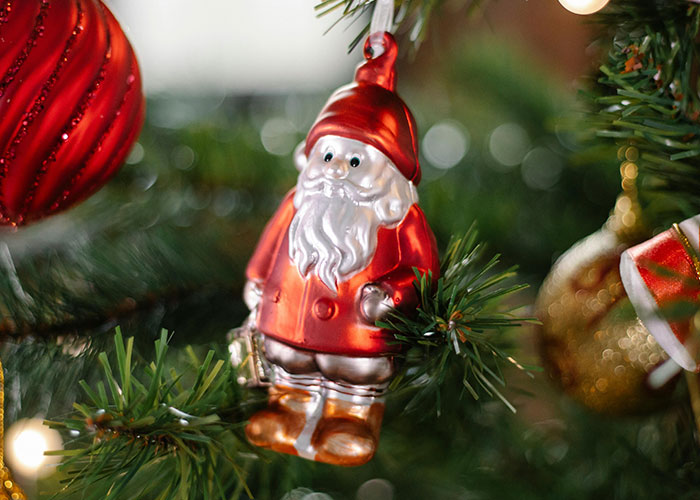 Santa Claus ornament hanging on a Christmas tree surrounded by festive decorations in a cozy holiday setting.