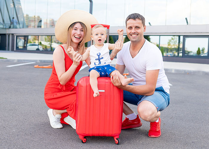 Happy family outdoors with toddler sitting on red suitcase, showcasing unhinged mom hacks blending genius and chaos.