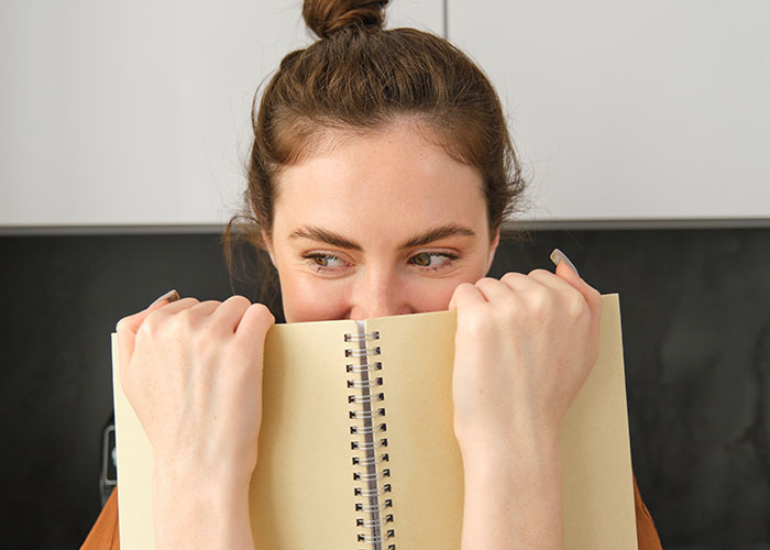 Young woman with hair bun holding a notebook close to her face, showcasing unhinged mom hacks that blend genius and chaos.