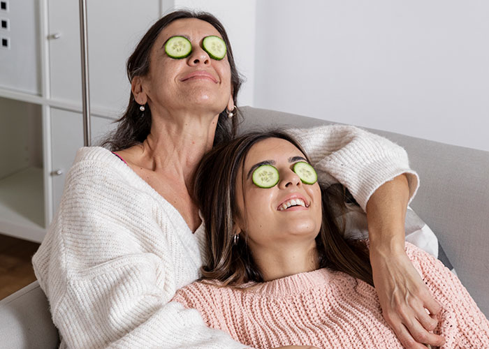 Two women relaxing with cucumber slices on their eyes, demonstrating unhinged mom hacks with a mix of genius and chaos.